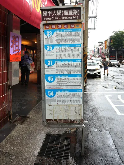 The pole at the Feng Chia U. (Fuxing Rd.) stop: circled numbers for the routes this pole carries, and below them each route's stop list and departure timetable panel.
